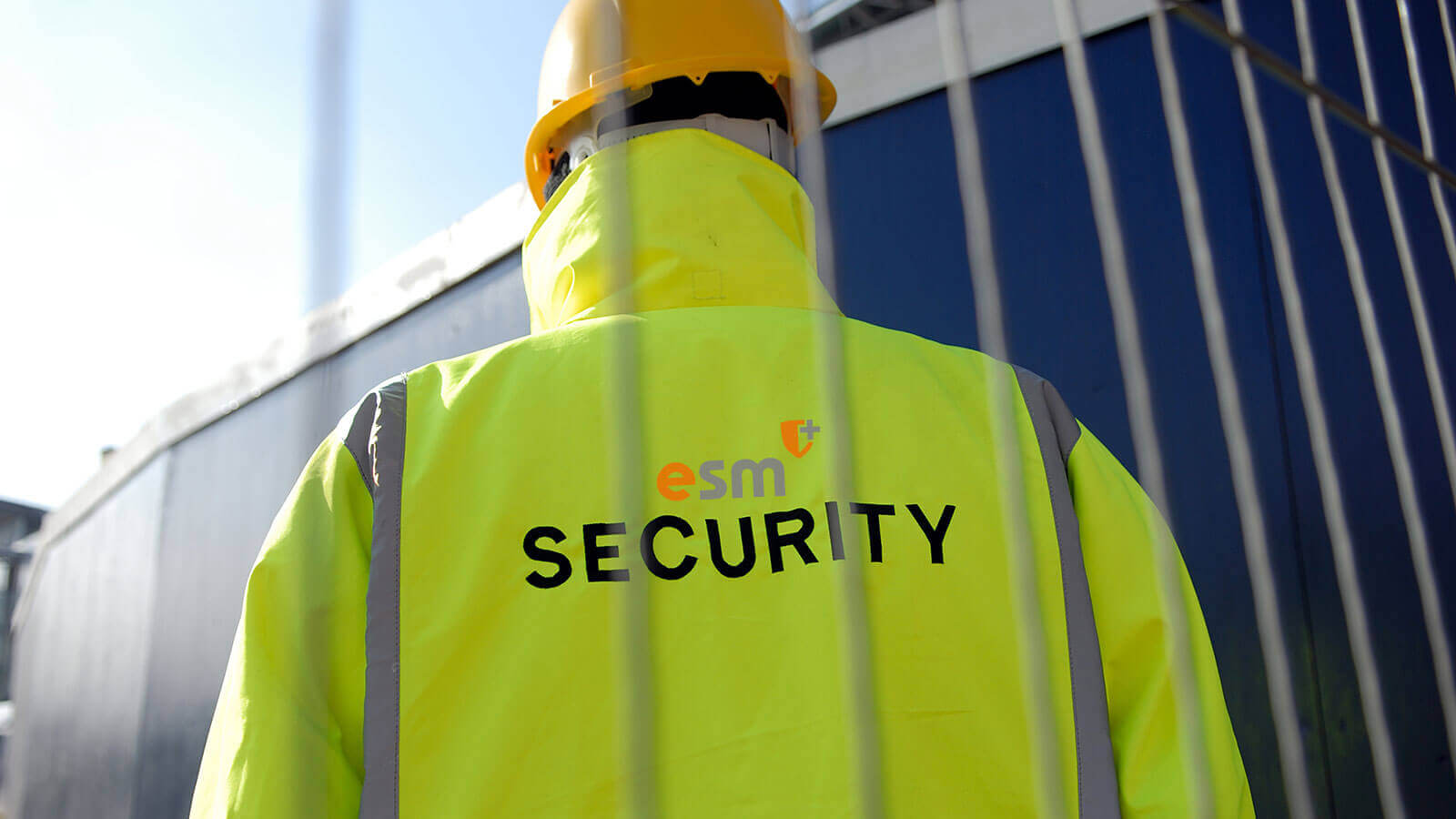 Security guard on site with hard hat and high visibility vest on with the ESM logo and Security written on the back